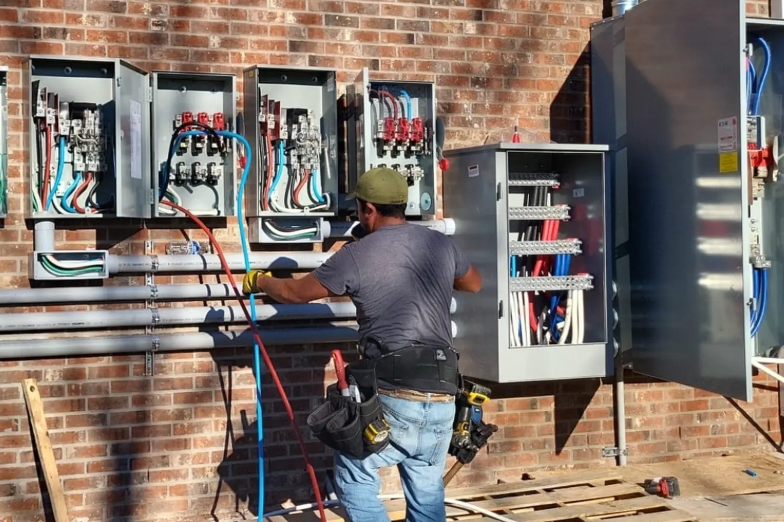 Electrician installing commercial electrical panels and conduit on a brick building