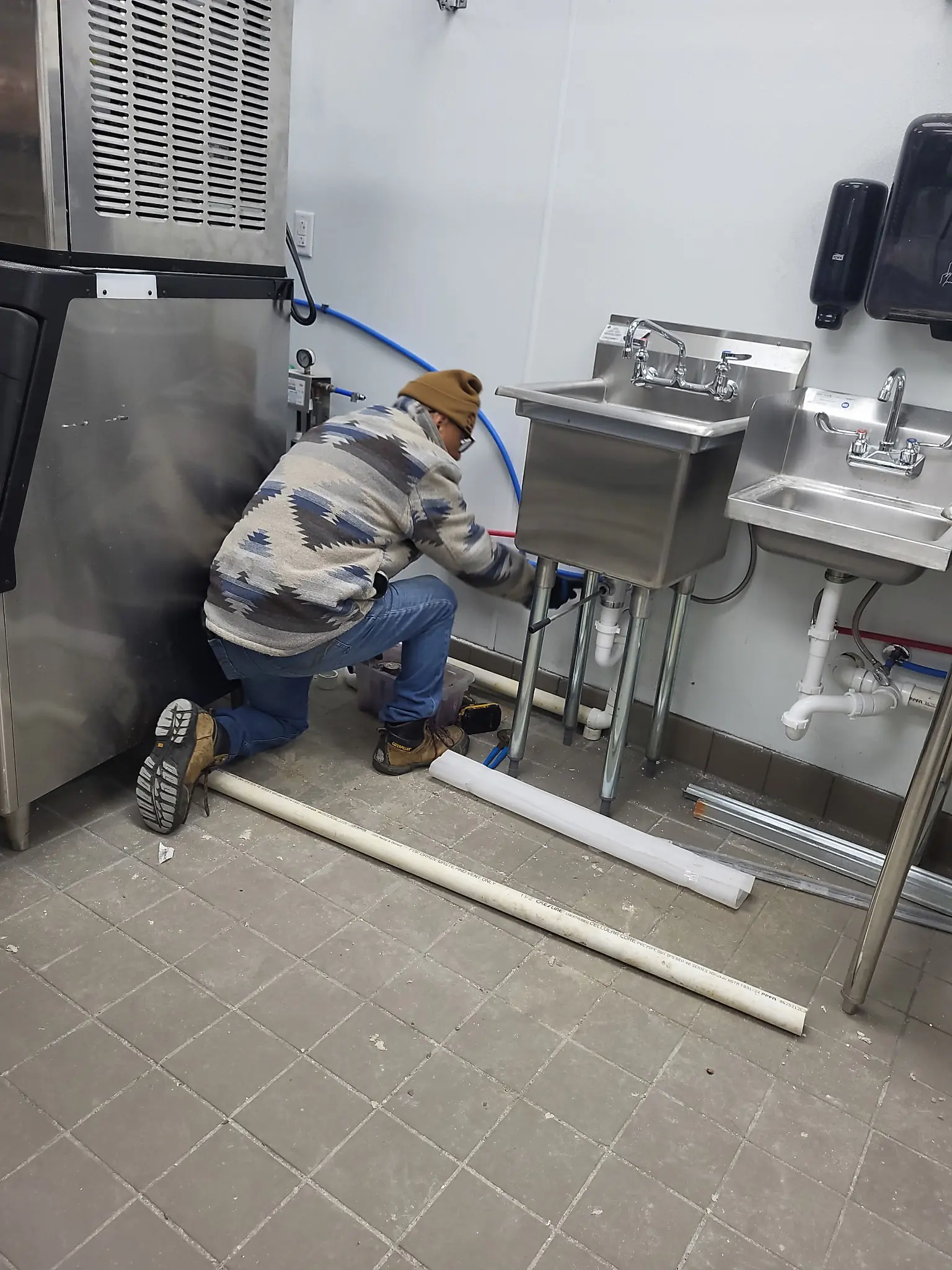 Modern Plumbing Systems technician servicing exposed piping beneath commercial sinks